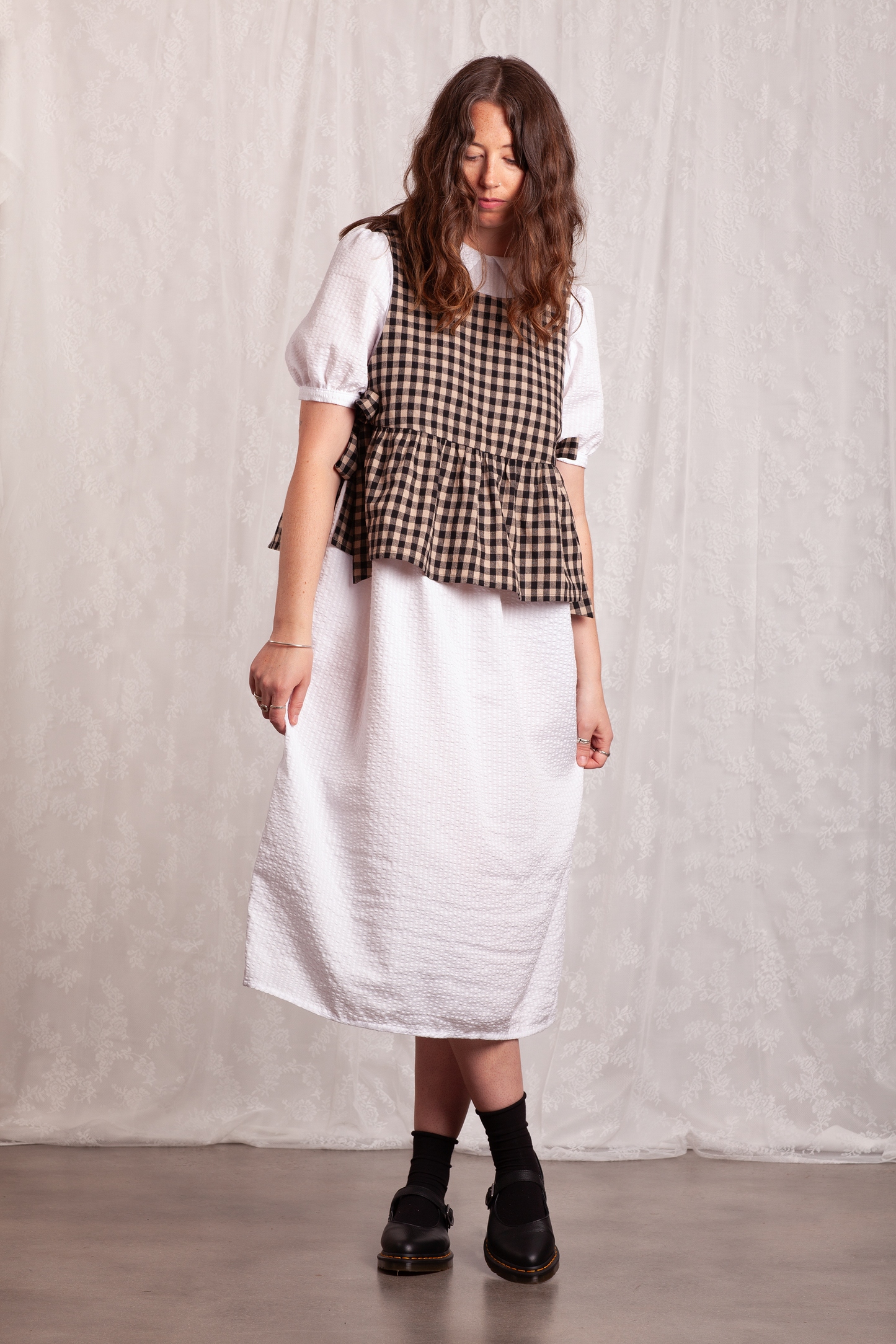 Woman wearing a white dress and gingham Poppy Apron Top with a plain background. Buy the Poppy Apron Top PDF sewing pattern. 