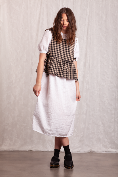 Woman wearing a white dress and gingham Poppy Apron Top with a plain background. Buy the Poppy Apron Top PDF sewing pattern. 