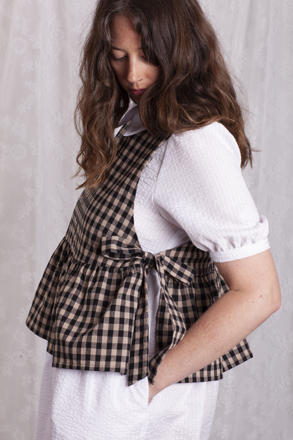Close up side view of woman wearing a white dress and green stripe Poppy Apron Top with a plain background. Buy the Poppy Apron Top PDF sewing pattern. 