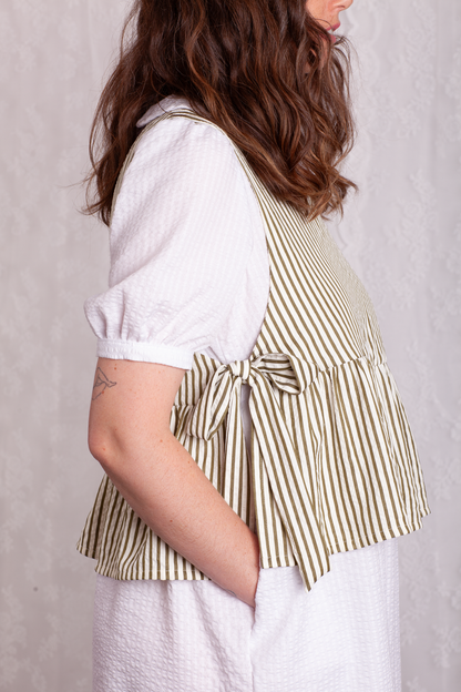 Close up side view of woman wearing a white dress and green stripe Poppy Apron Top with a plain background. Buy the Poppy Apron Top PDF sewing pattern. 
